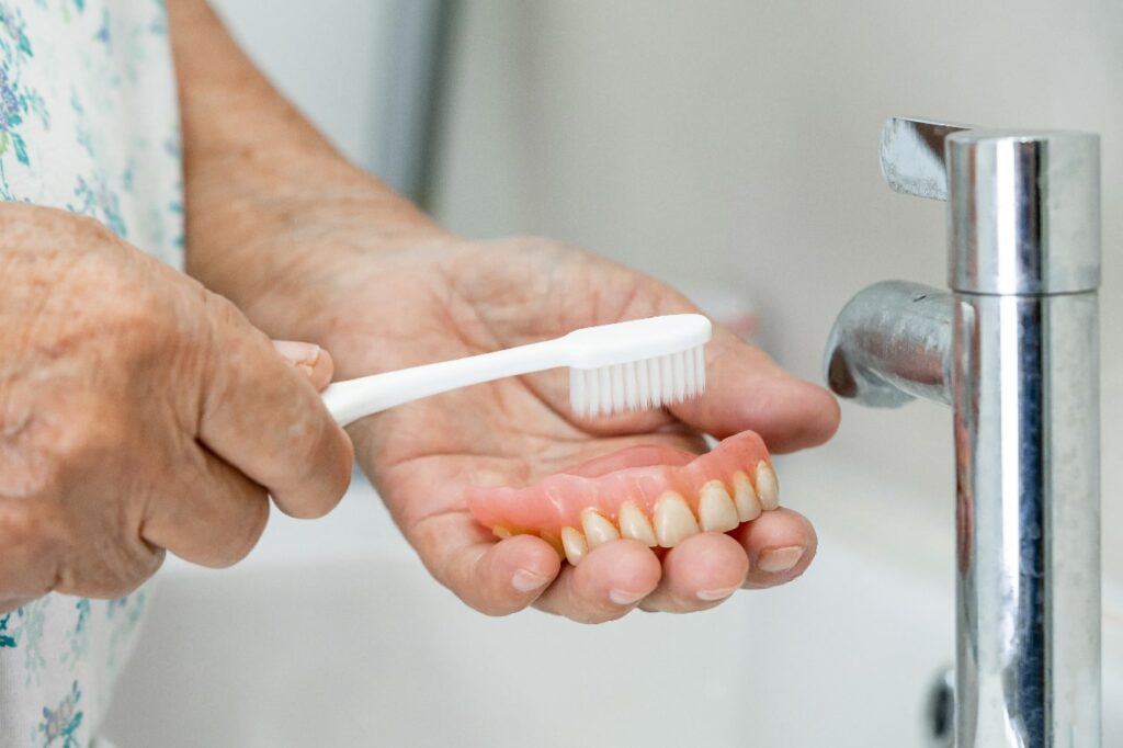 Asian senior or elderly old woman patient use toothbrush to clean partial denture of replacement teeth